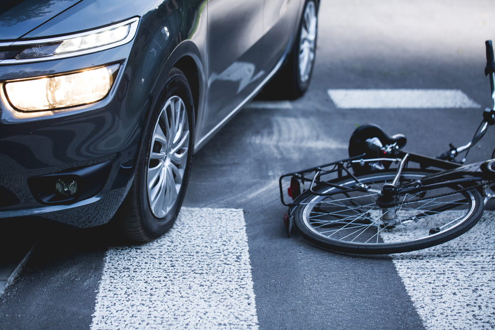 Car stopped beside a fallen bicycle in a marked crosswalk.