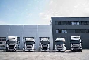 Line of new modern white trucks parked outside a sleek, industrial warehouse
